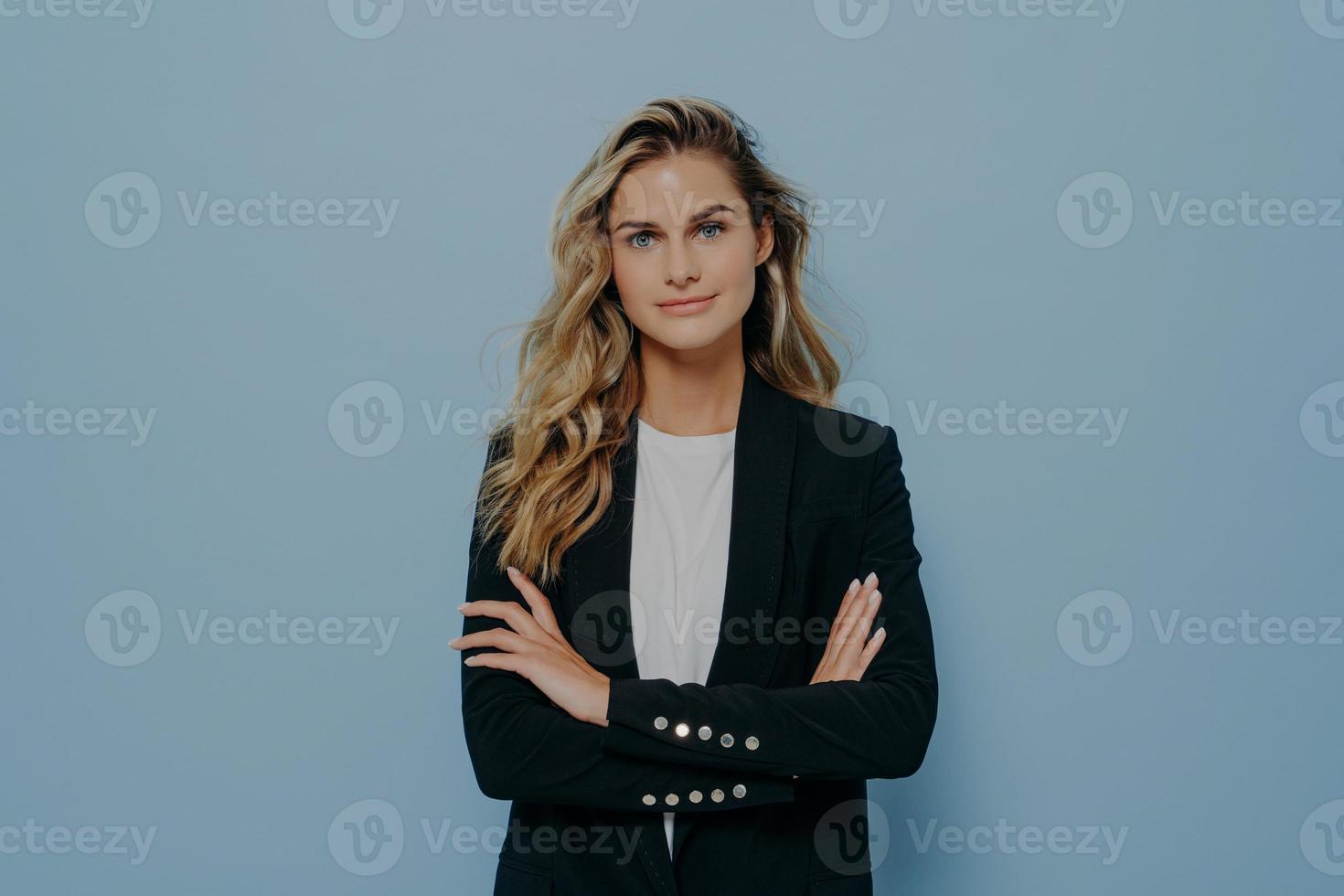 Young confident blonde business woman dressed in smart black costume standing with crossed arms photo