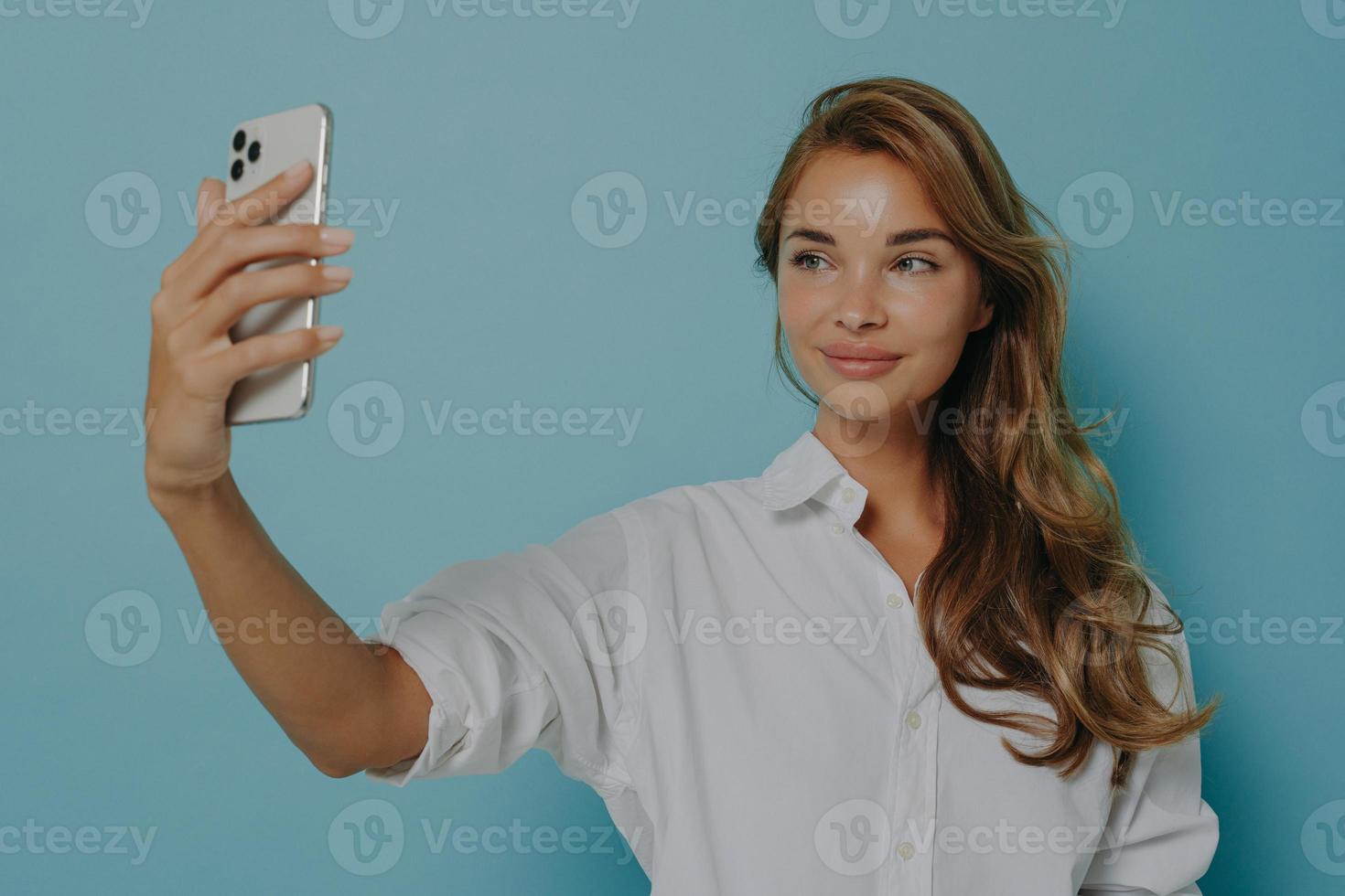 mujer con cabello largo toma selfie a través de un teléfono inteligente moderno toma una foto de sí misma hace una videollamada