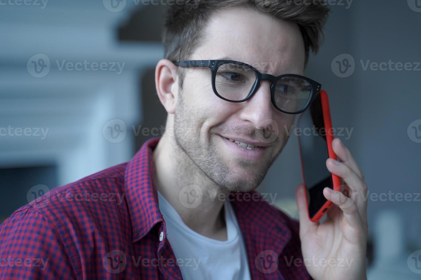 Young smiling german guy in glasses using mobile phone and talking on with friend photo