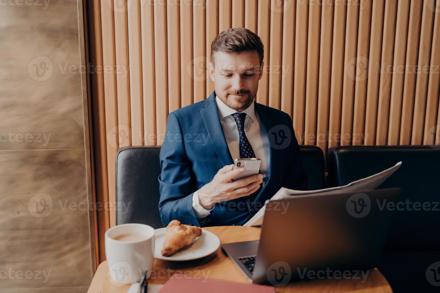 joven empresario confiado en ropa formal disfrutando del café y trabajando de forma remota en el café foto