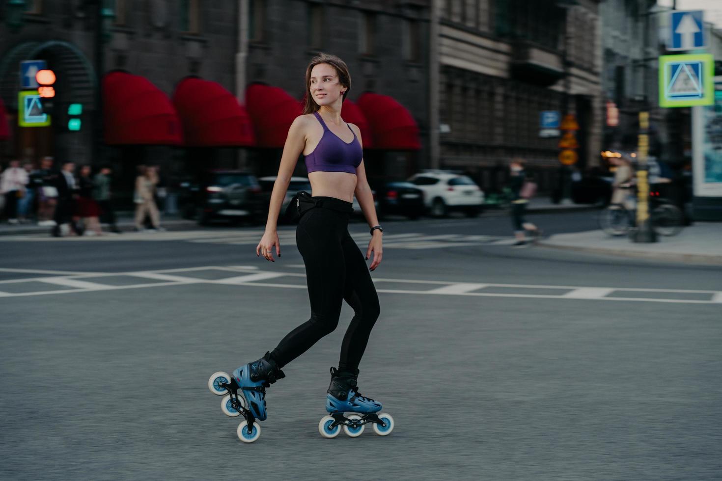 Full length shot of active slim young woman dressed in sportsclothes rides on rollers to strengthen arms and legs muscles improves balance agility and coordination has good mood burns calories photo