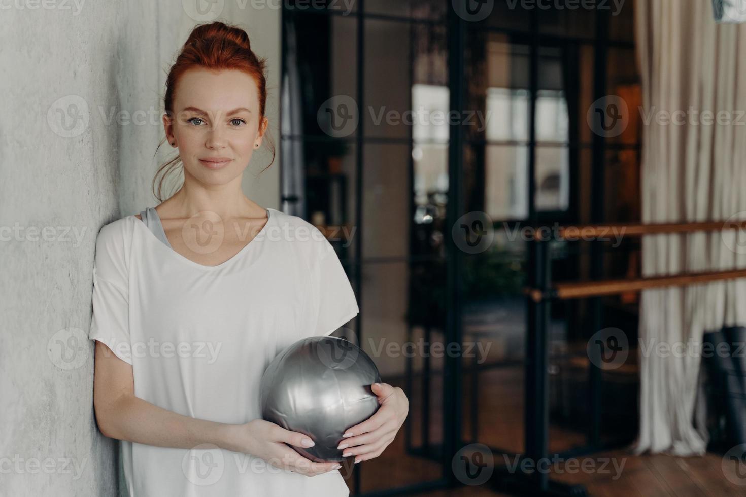 Young sporty lady with red hair resting during workout in fitness studio photo