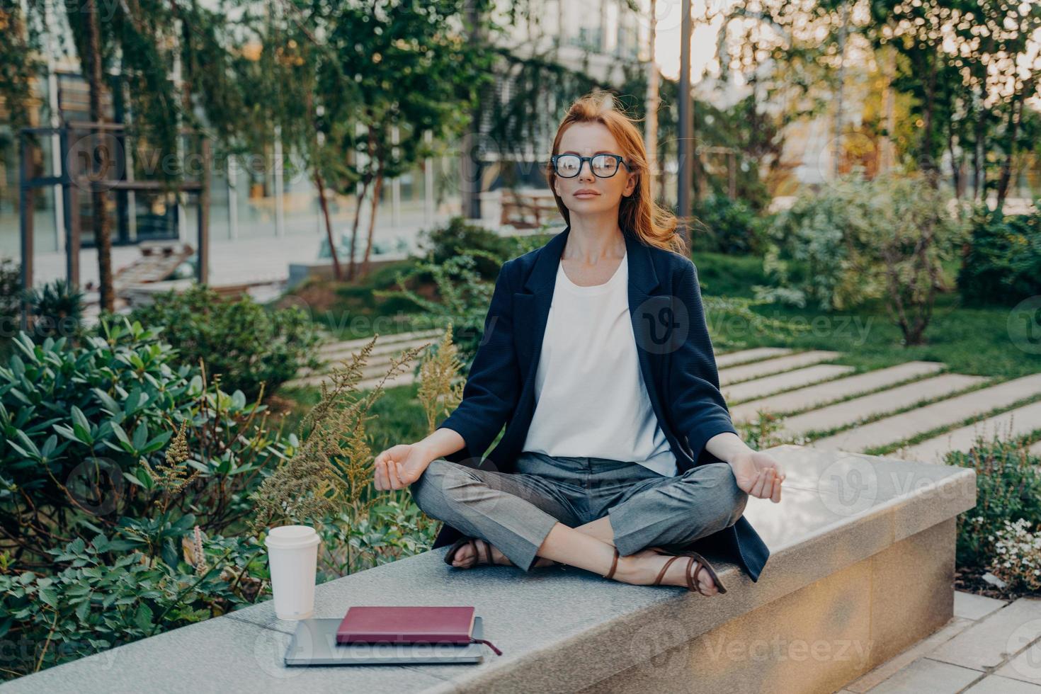 Relaxed redhead young woman does yoga outside sits in lotus pose poses in park photo