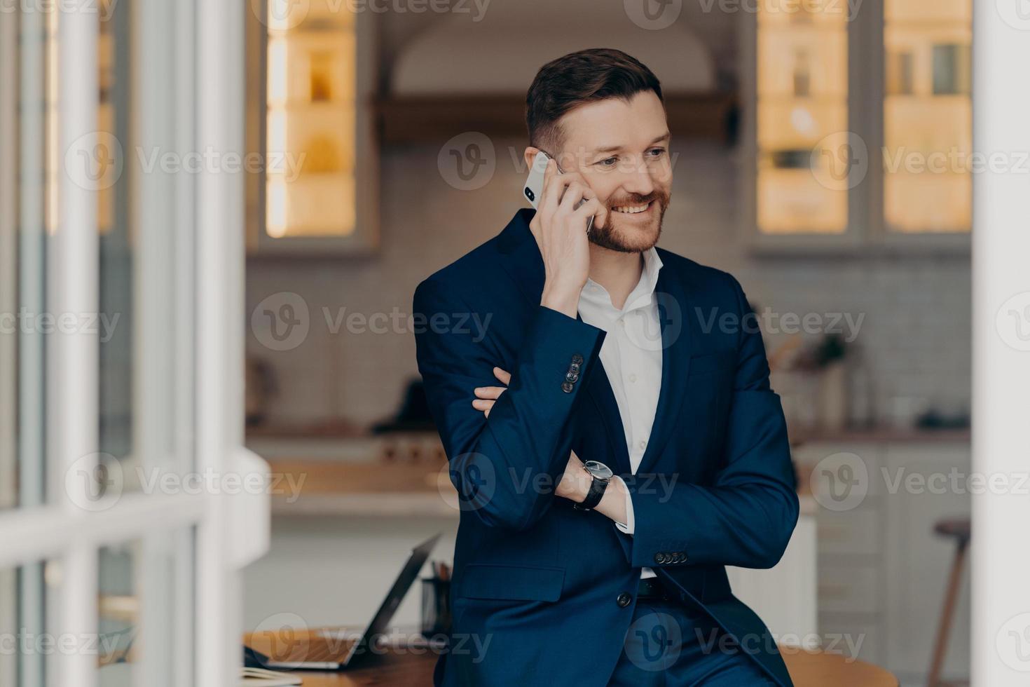 hombre de negocios sonriente con traje azul oscuro hablando por teléfono móvil foto
