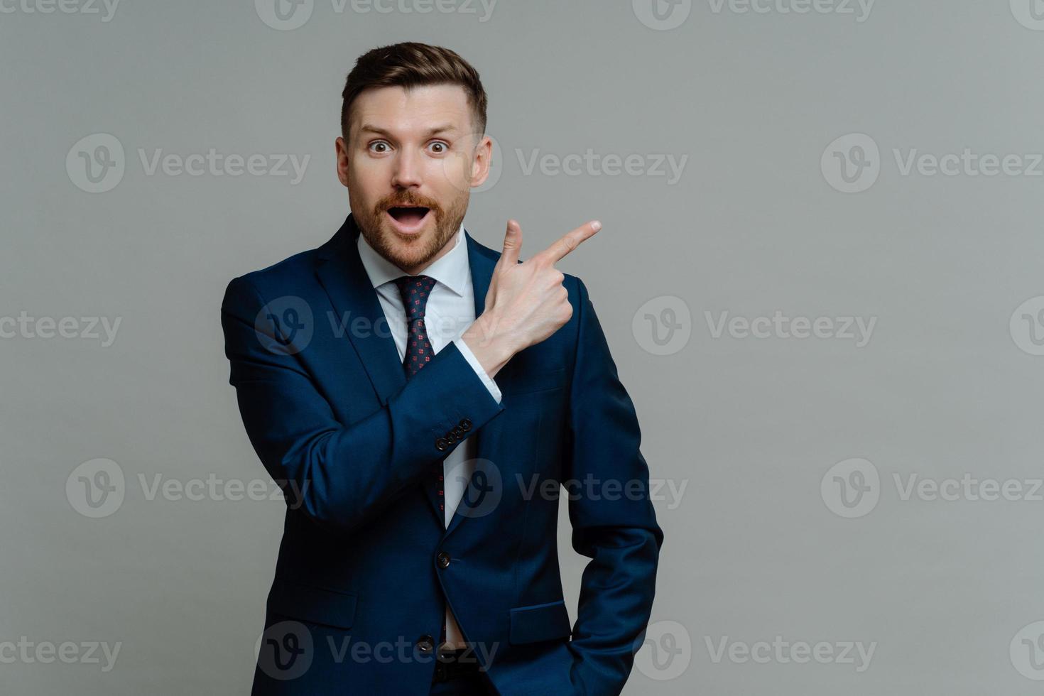 sorprendido elegante empresario empoyee anuncia copia espacio vestido con traje formal aislado sobre fondo de estudio gris. empresario exitoso promueve su producto o servicio. mejor elección foto