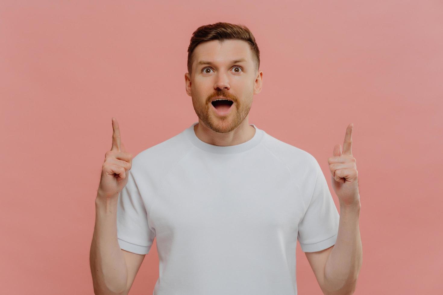 Excited young man pointing with two forefingers up and with shocked face expression photo