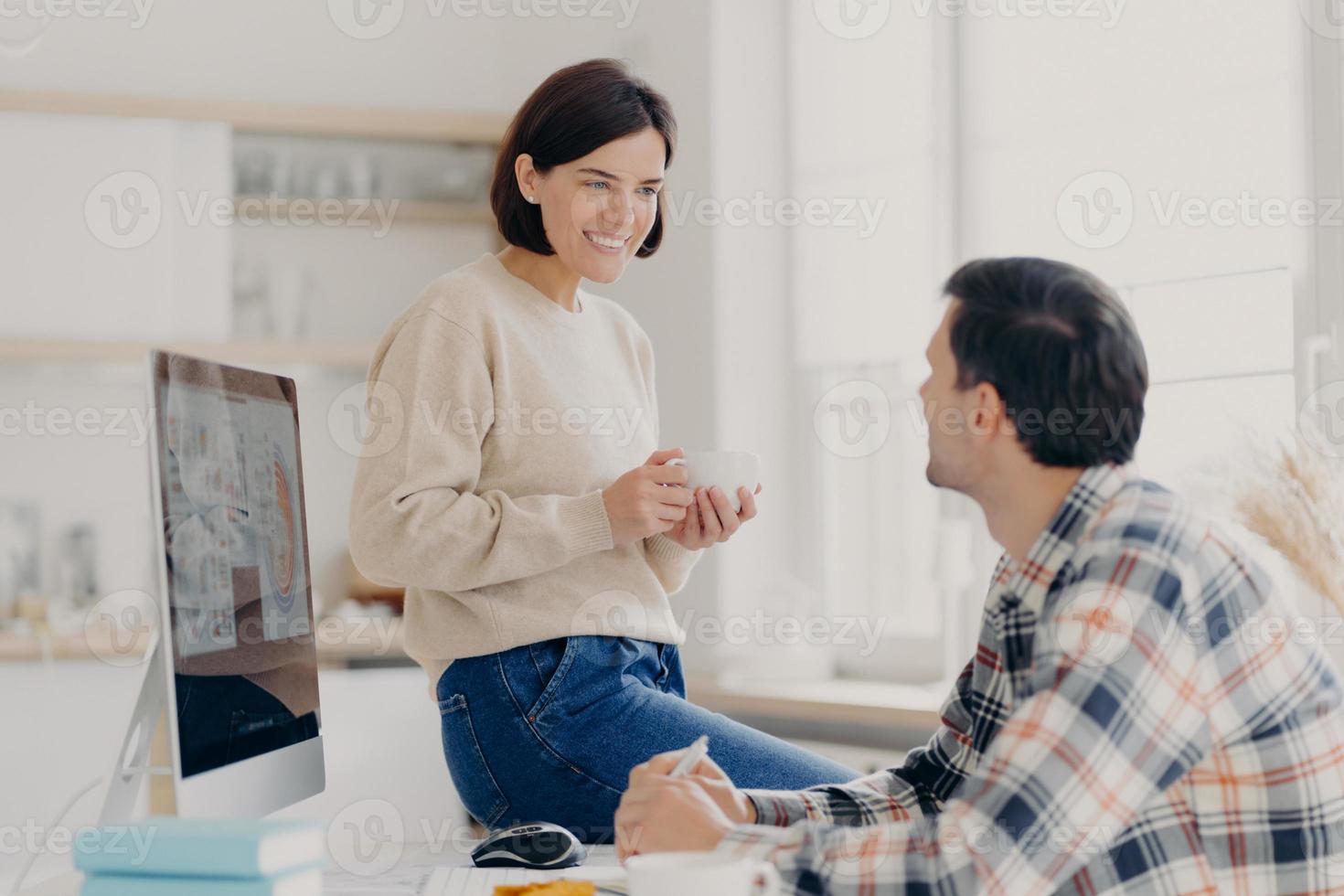 Family couple discusses making future investments, pose in coworking space, work on modern computer, look happily at each other during coffee break, want to make purchase, work remotely at home photo