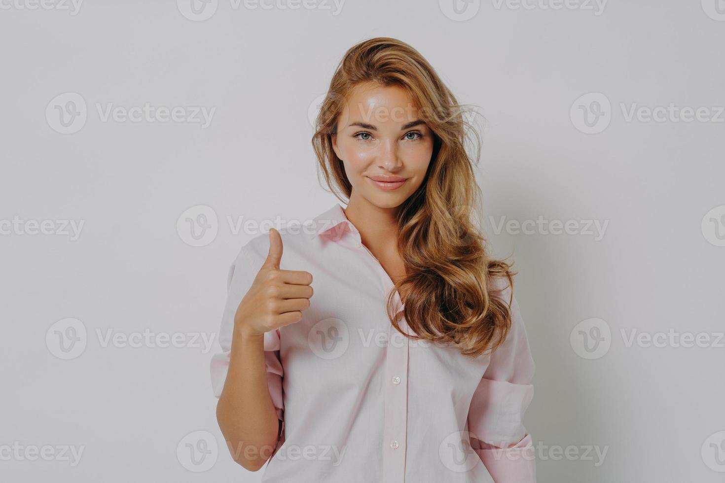 Enthusiastic young Caucasian woman keeps thumb up recommends something very good says yes photo