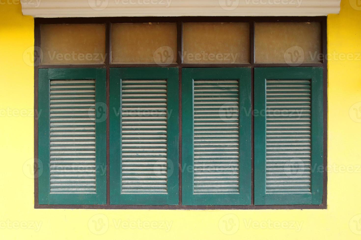 fila de ventanas retro de color verde oscuro en forma de rectángulo y pared amarilla brillante de la casa en tailandia. foto