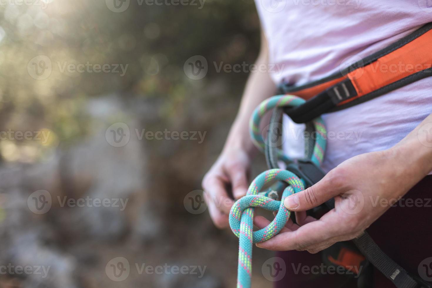 A rock climber prepares equipment for climbing, woman holds a rope, knot photo