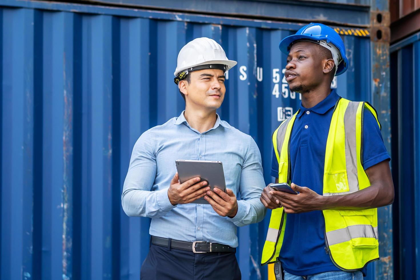 Port manager and engineer while standing by freight containers on a large commercial dock discussing shipping logistics together photo