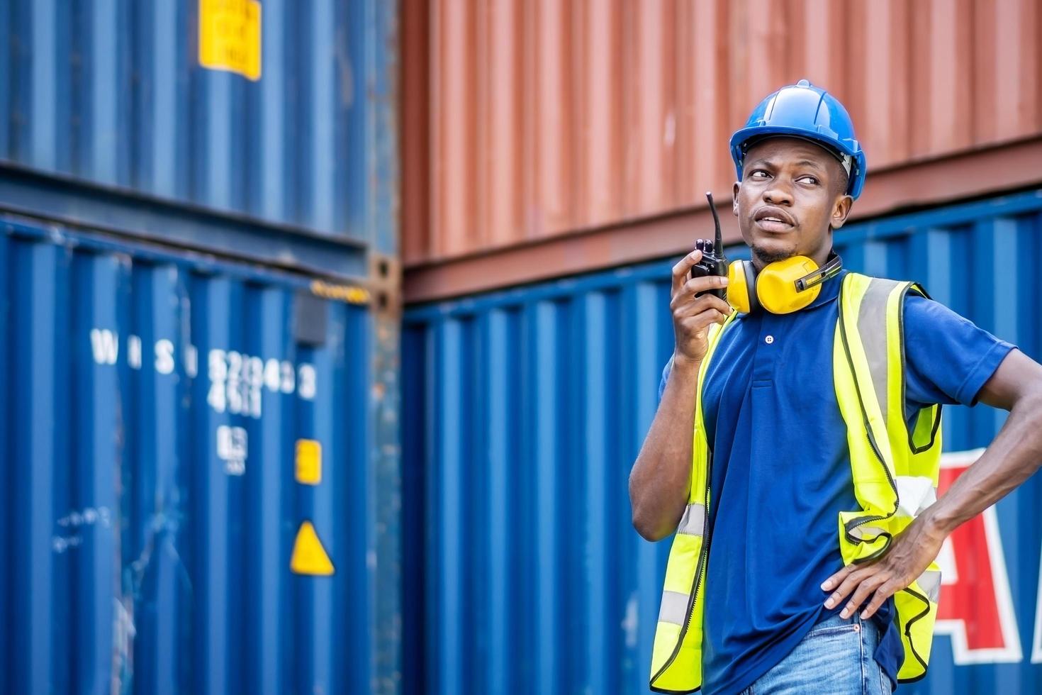 Adult African american men worker Check and control loading freight Containers by use radio at commercial shipping dock feeling curious. Cargo freight ship for import export concept photo