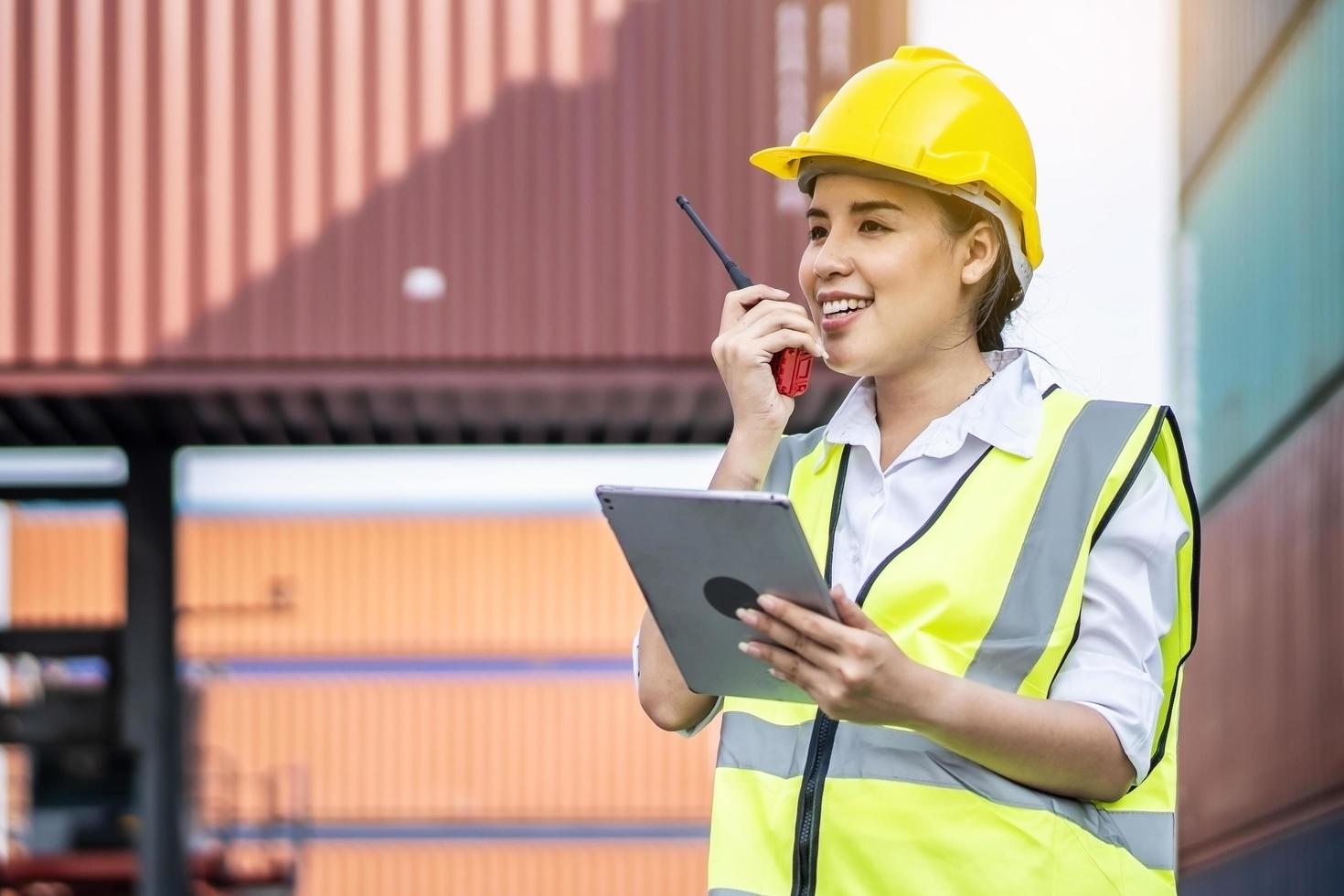 joven ingeniera o gerente asiática que sostiene una tableta y usa comunicación por radio para controlar la carga de contenedores en conceptos de logística y transporte industrial foto