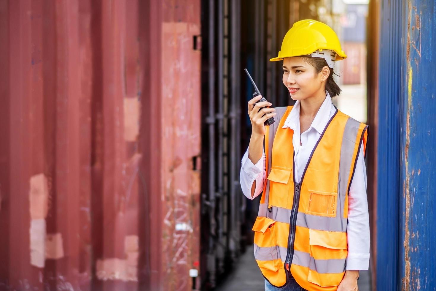 joven ingeniera segura de sí misma sonriendo y usando comunicación por radio y usando casco de seguridad amarillo y verificando el control de la caja de contenedores de carga del buque de carga para importación y exportación foto