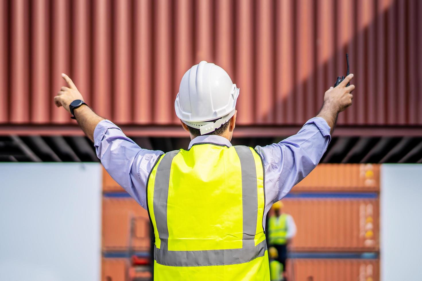 Rear view of engineer in reflective clothing with safety helmet is working and checking at containers cargo on shipping port area at harbor photo