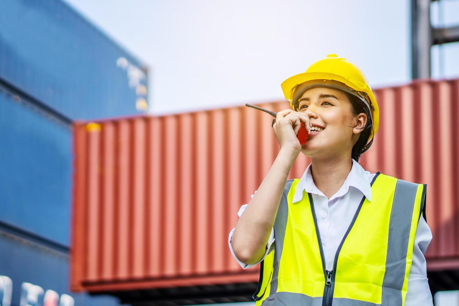 joven ingeniera segura de sí misma sonriendo y usando comunicación por radio y usando casco de seguridad amarillo y verificando el control de la caja de contenedores de carga del buque de carga para importación y exportación foto