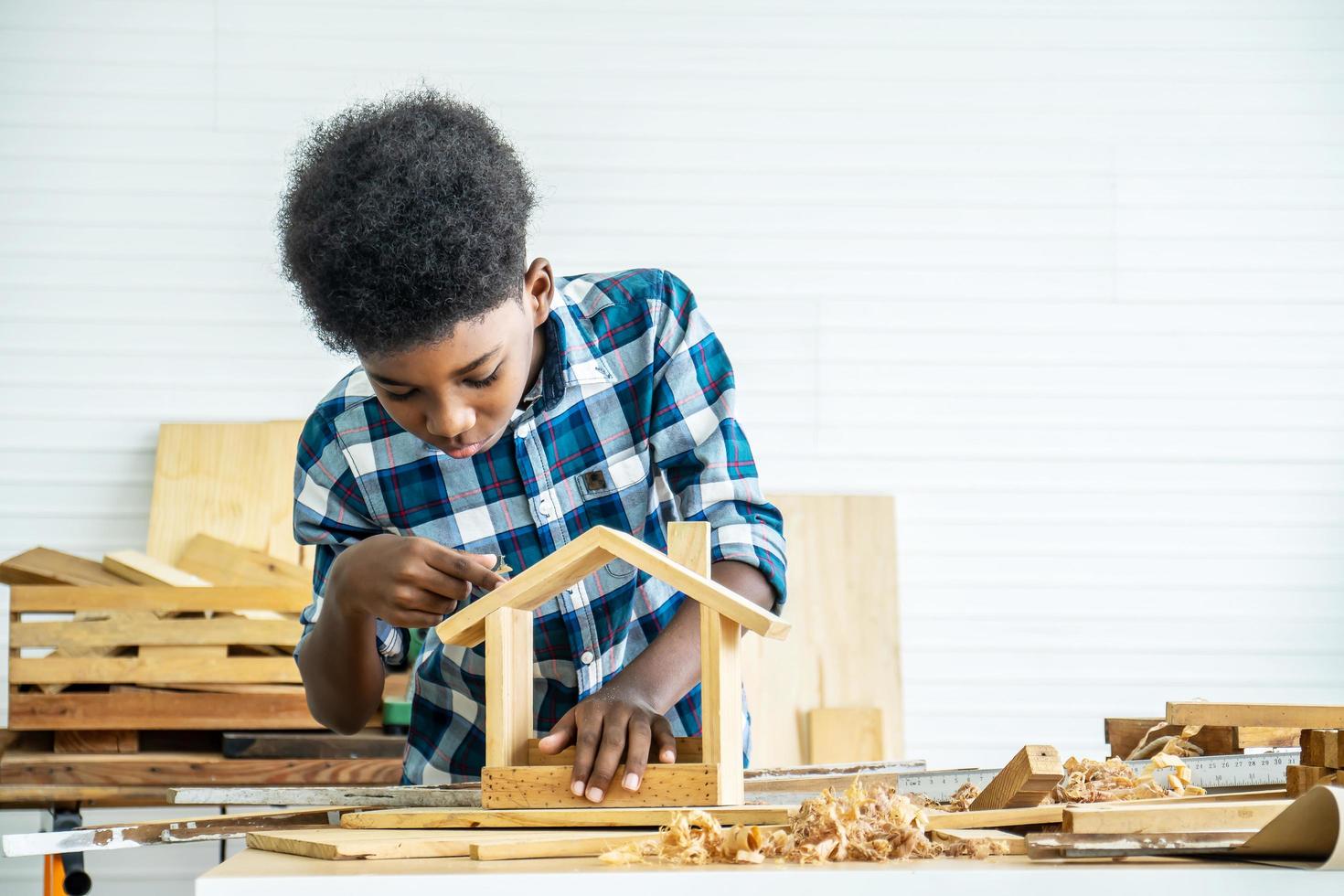 niño sonriente carpintero feliz trabajando con madera y papel de lija foto