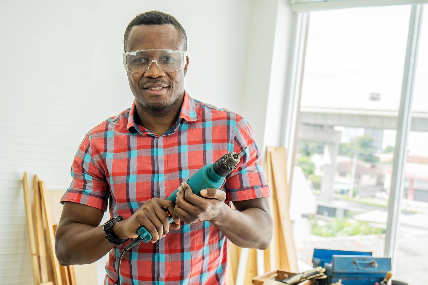 Work in the carpentry workshop. African american happy male holds a screwdriver in his hand. human in a woodworking workshop. Builder at the workplace. Carpenter poses in the workplace. photo