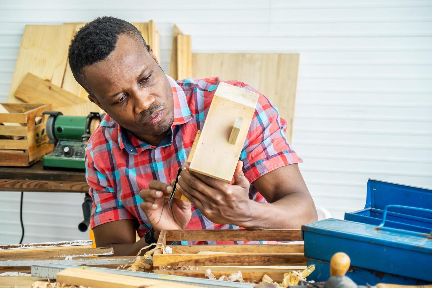 Young carpenter african american man using sandpaper on a piece of  House made of wood for furniture in workshop photo