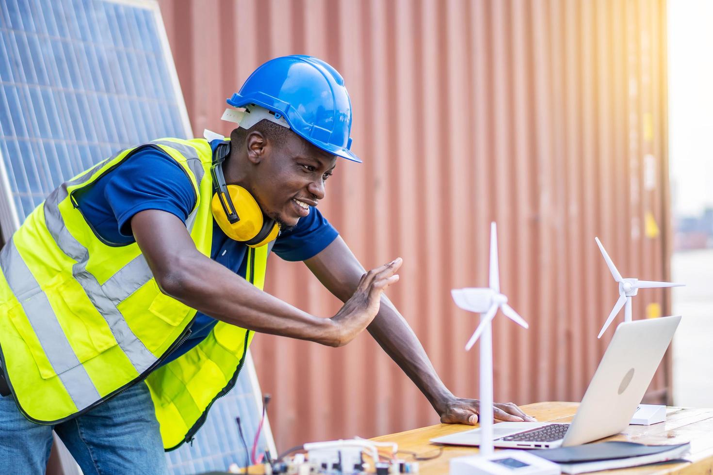 un ingeniero masculino que usa una computadora portátil, hace una videollamada al cliente o socio comercial por las negociaciones fueron exitosas., en el escritorio hay modelos de molinos de viento. concepto de desarrollo sostenible foto