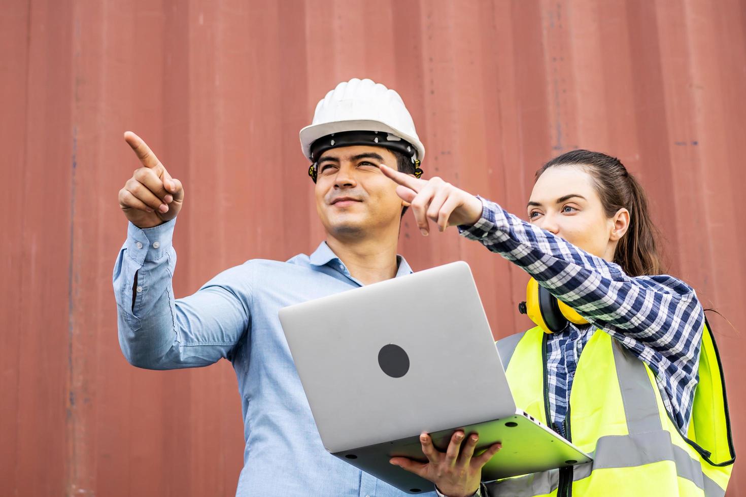 Confident foreman and engineers while standing point to position loading Containers box from Cargo freight ship at Cargo container shipping on a large commercial shipping dock photo