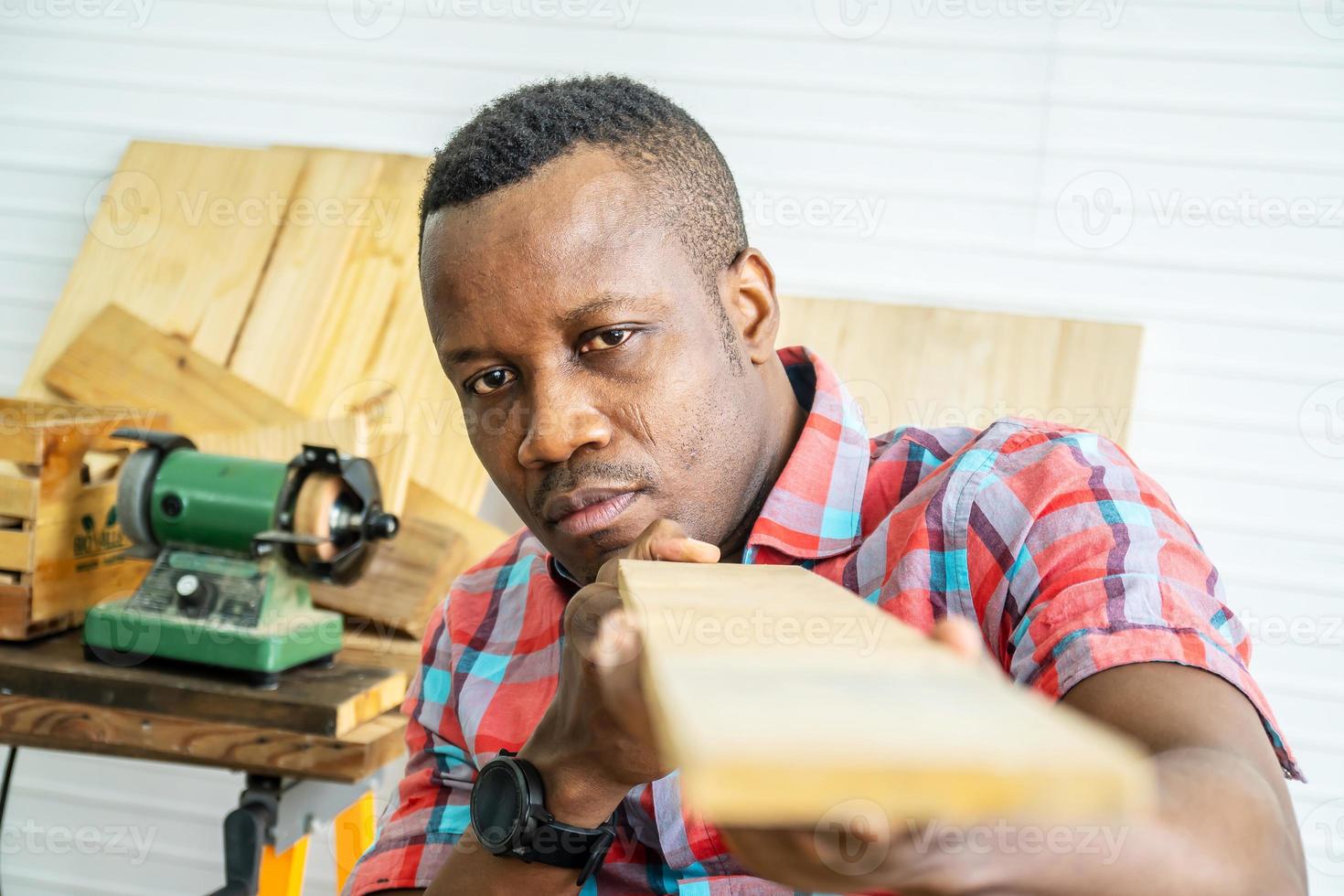 Young carpenter african american man looking and choosing wood and using sandpaper to rub wooden plank at workshop table in carpenter wood factory photo