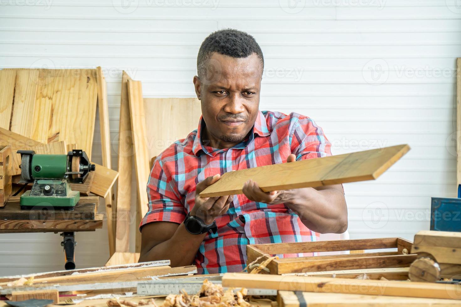 Young carpenter african american man looking and choosing wood and using sandpaper to rub wooden plank at workshop table in carpenter wood factory photo