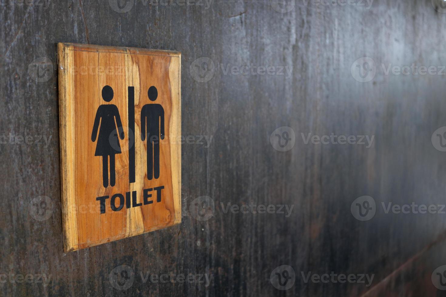 Toilet sign in wood frame on black painted metal wall. Some rusty and scratch on surface of wall. photo