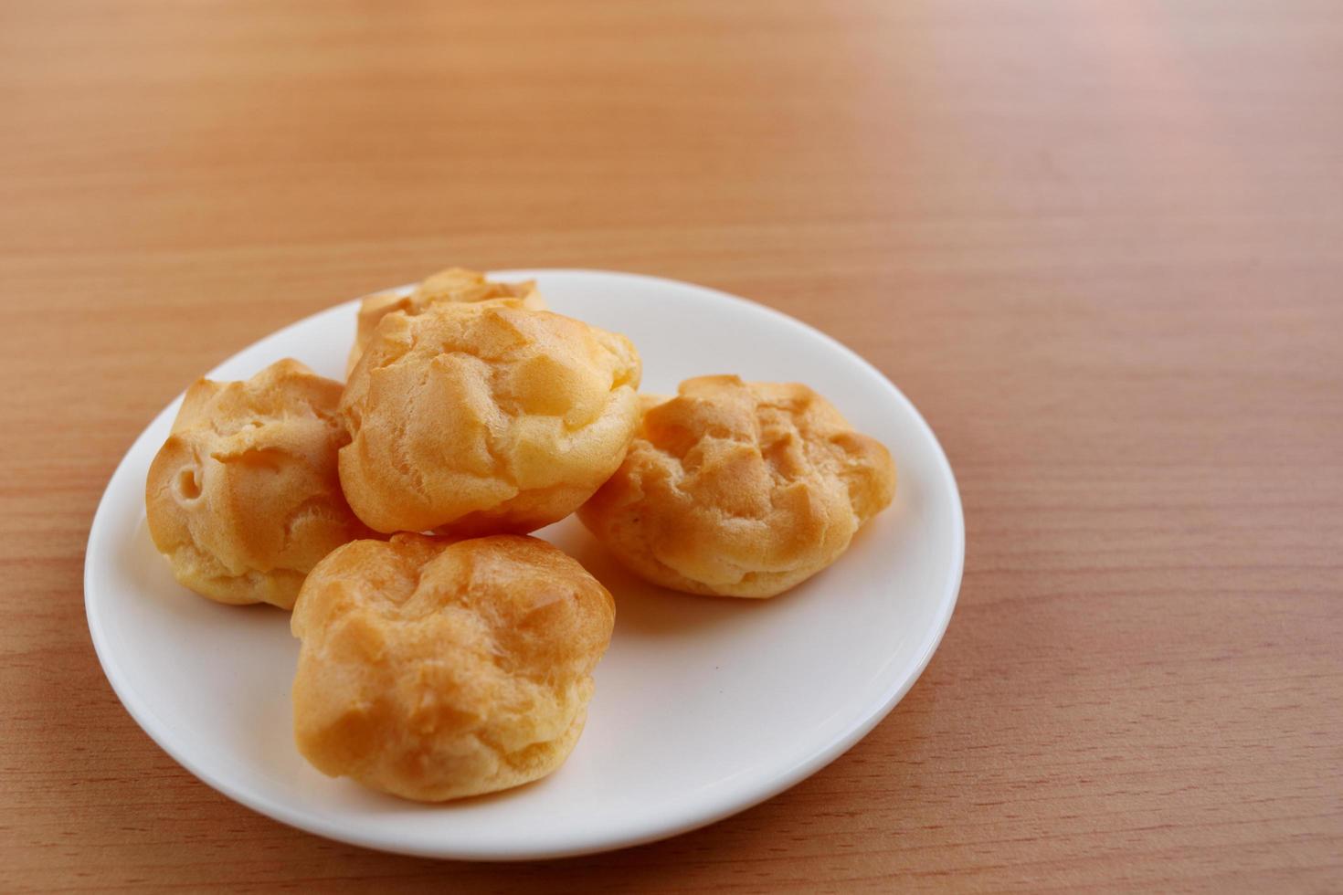 Group of round shape eclair on round white dish  and light brown wood background. Selective focus. photo