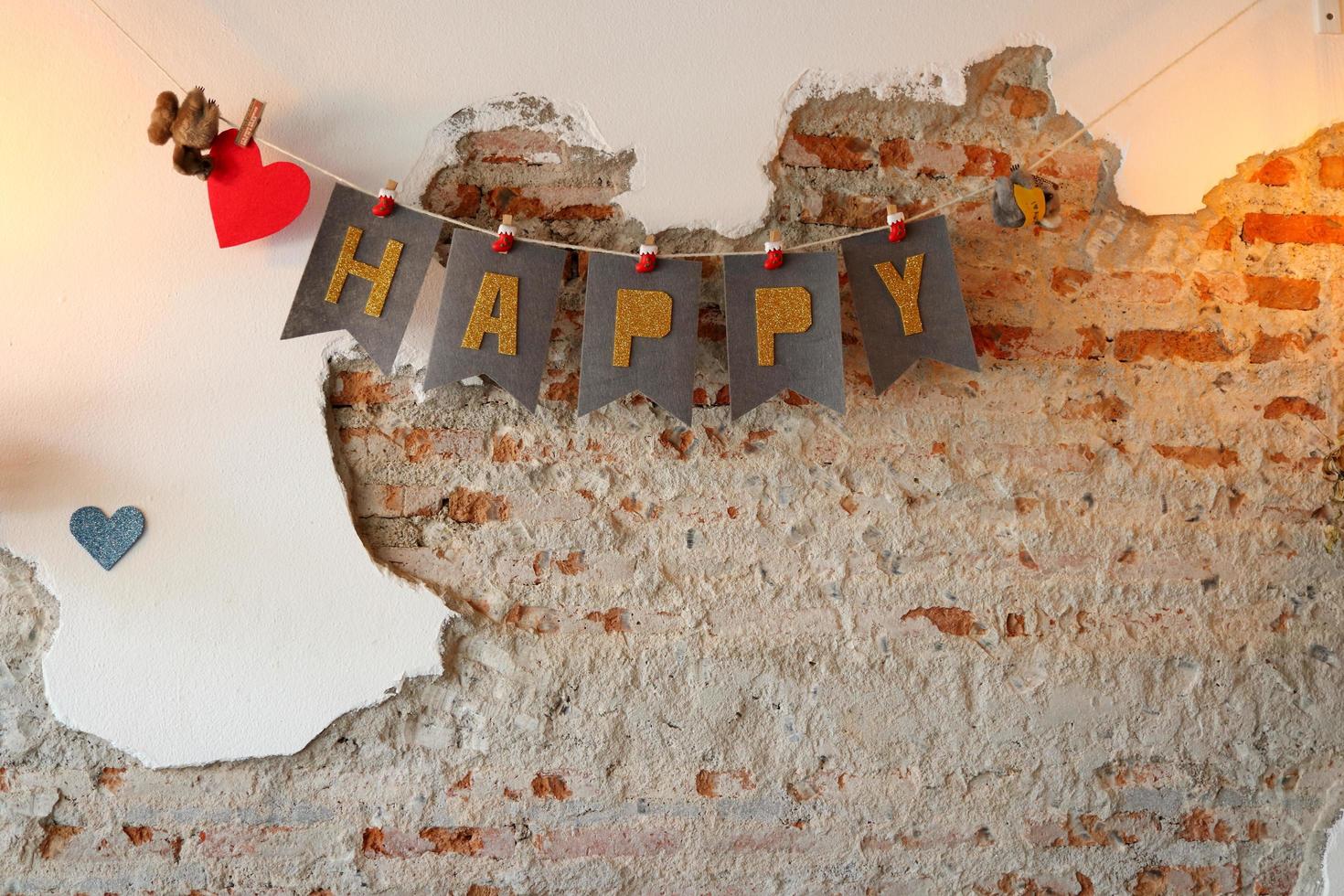 la palabra feliz colgando de alambre y cemento roto pintado de fondo de pared blanca abierta de ladrillo rojo en el interior. la letra es de color marrón sobre papel gris. foto