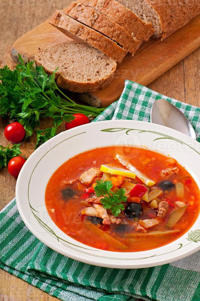 Soup solyanka Russian with meat, olives and gherkins in wooden bowl photo