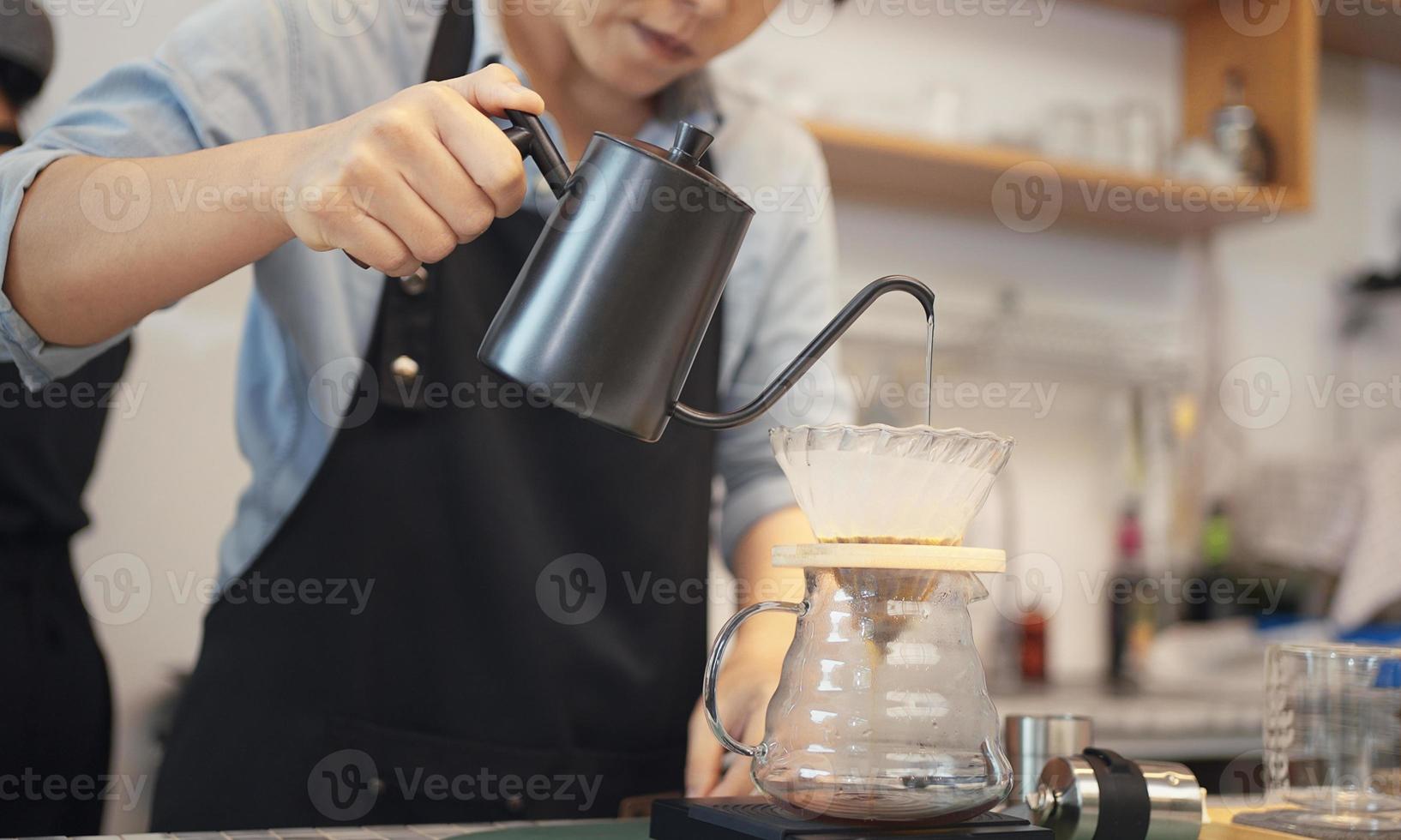 una operadora de café que usa un delantal vierte agua caliente sobre café tostado para preparar café para los clientes en la tienda. foto