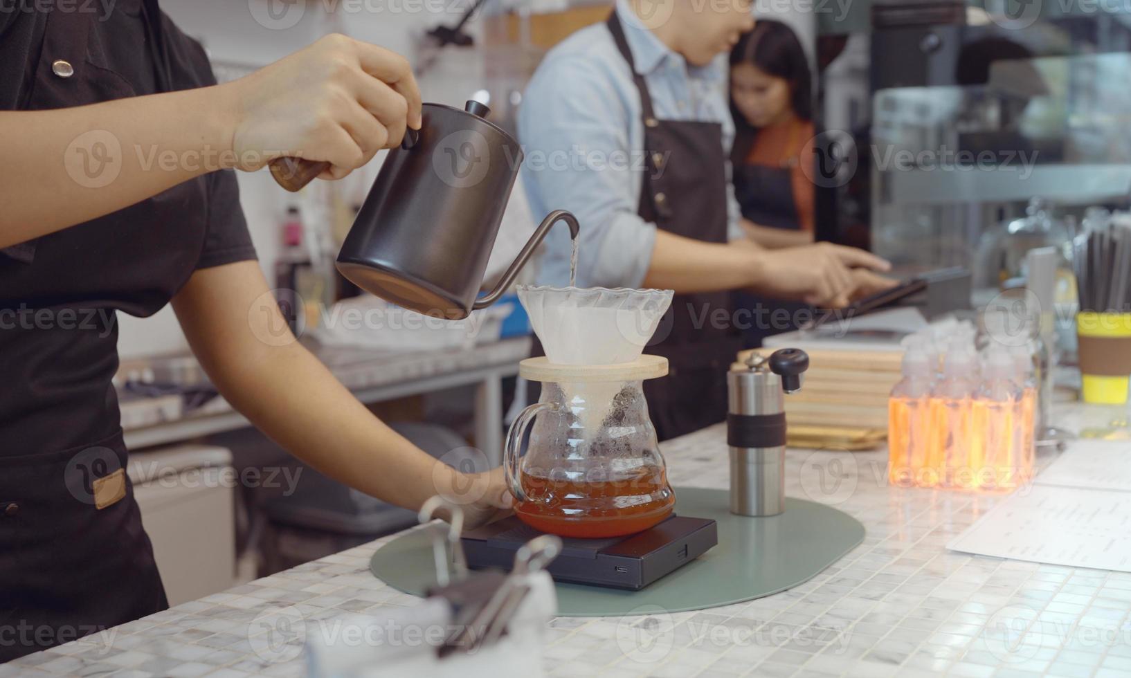 una operadora de café que usa un delantal vierte agua caliente sobre café tostado para preparar café para los clientes en la tienda. foto