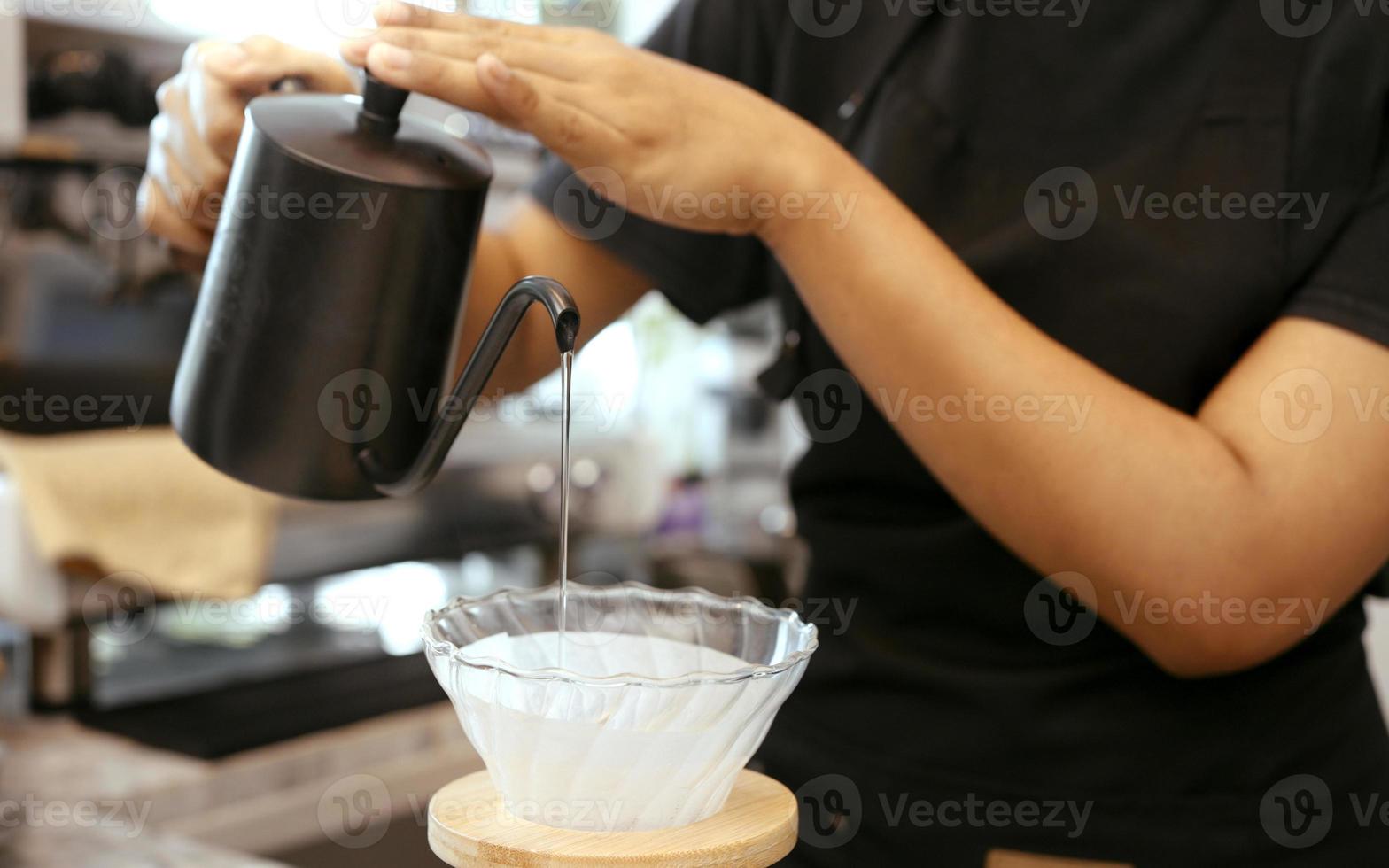 una operadora de café que usa un delantal vierte agua caliente sobre café tostado para preparar café para los clientes en la tienda. foto