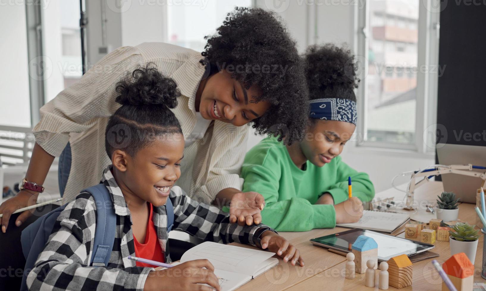 African American female teacher standing with pupils teaching writing lesson in modern classroom. photo