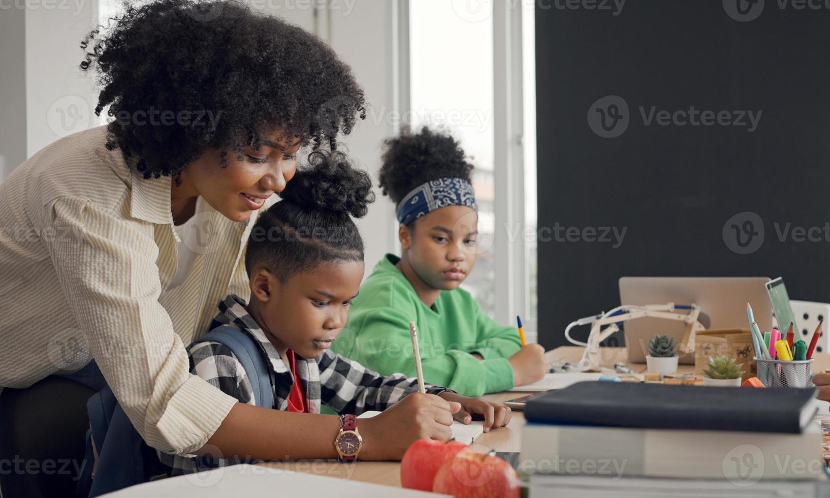 profesora afroamericana de pie con alumnos enseñando lecciones de escritura en un aula moderna. foto