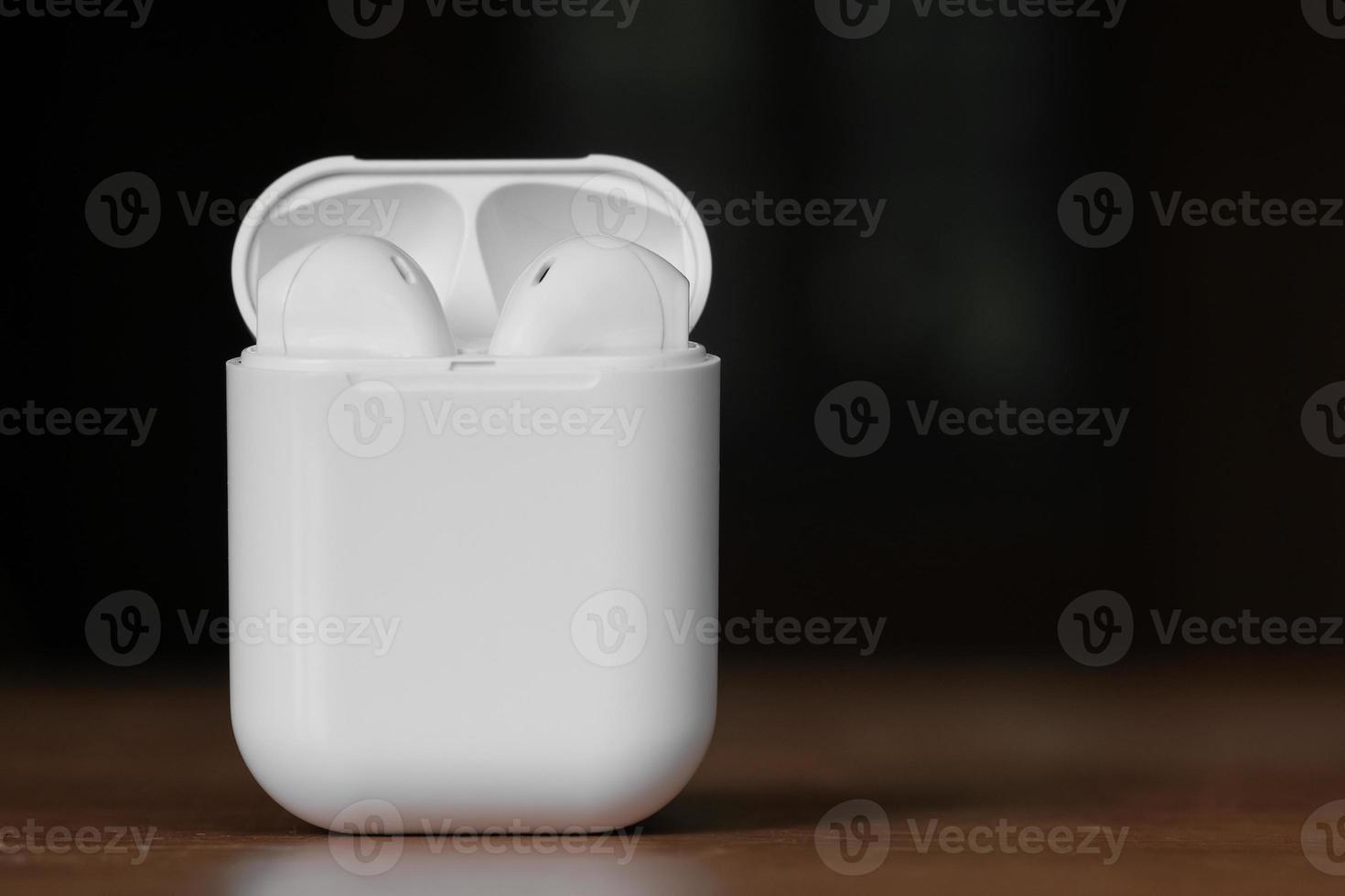 White color true wireless earphone in opened charging case ready for pairing on wooden table. Copy space. Selective focus. photo