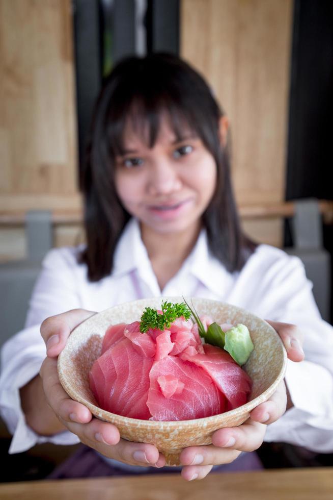 una adolescente muestra un don maguro o atún en un restaurante japonés. foto