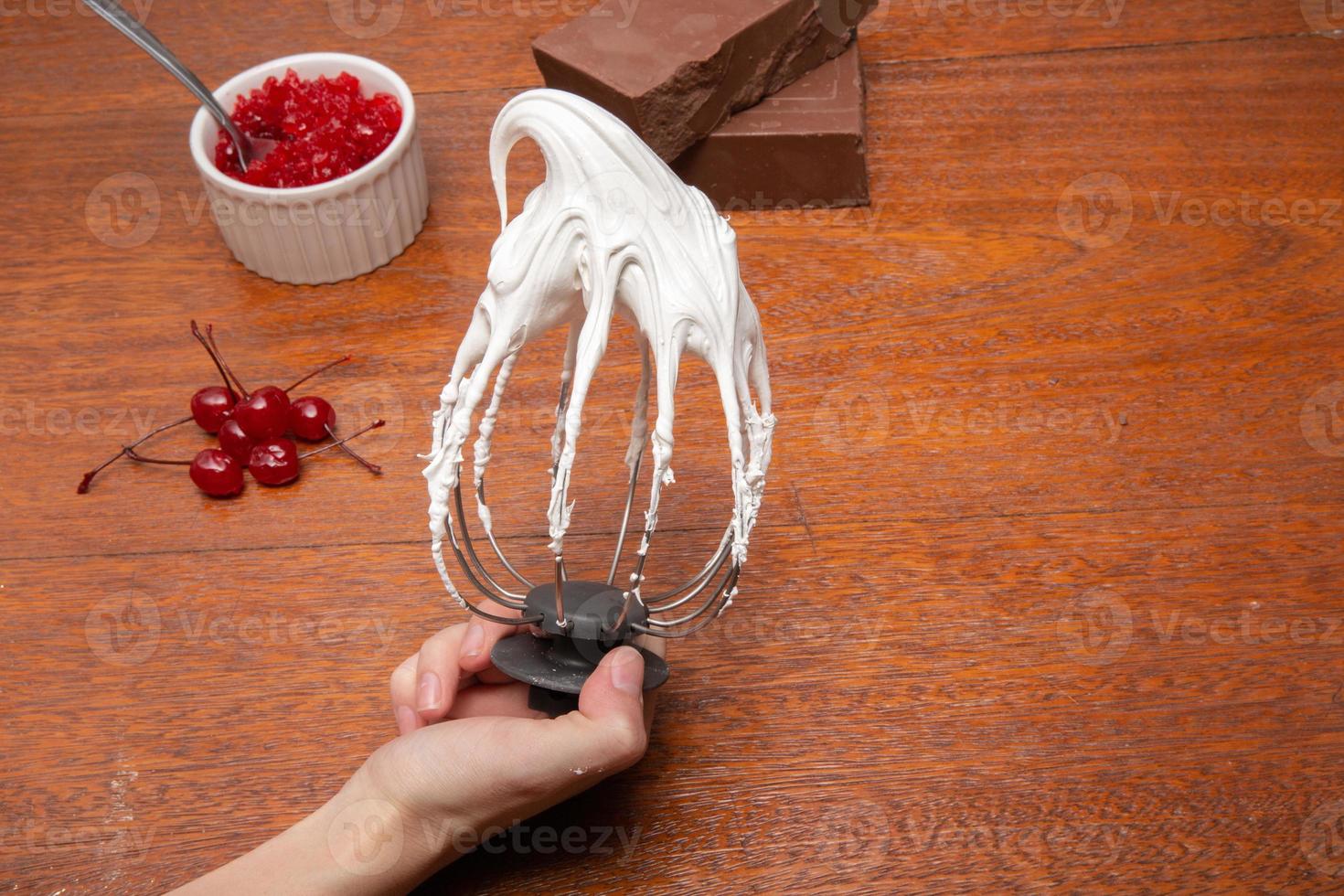 Metal whisk with whipped egg with shadows whites on wood table background photo