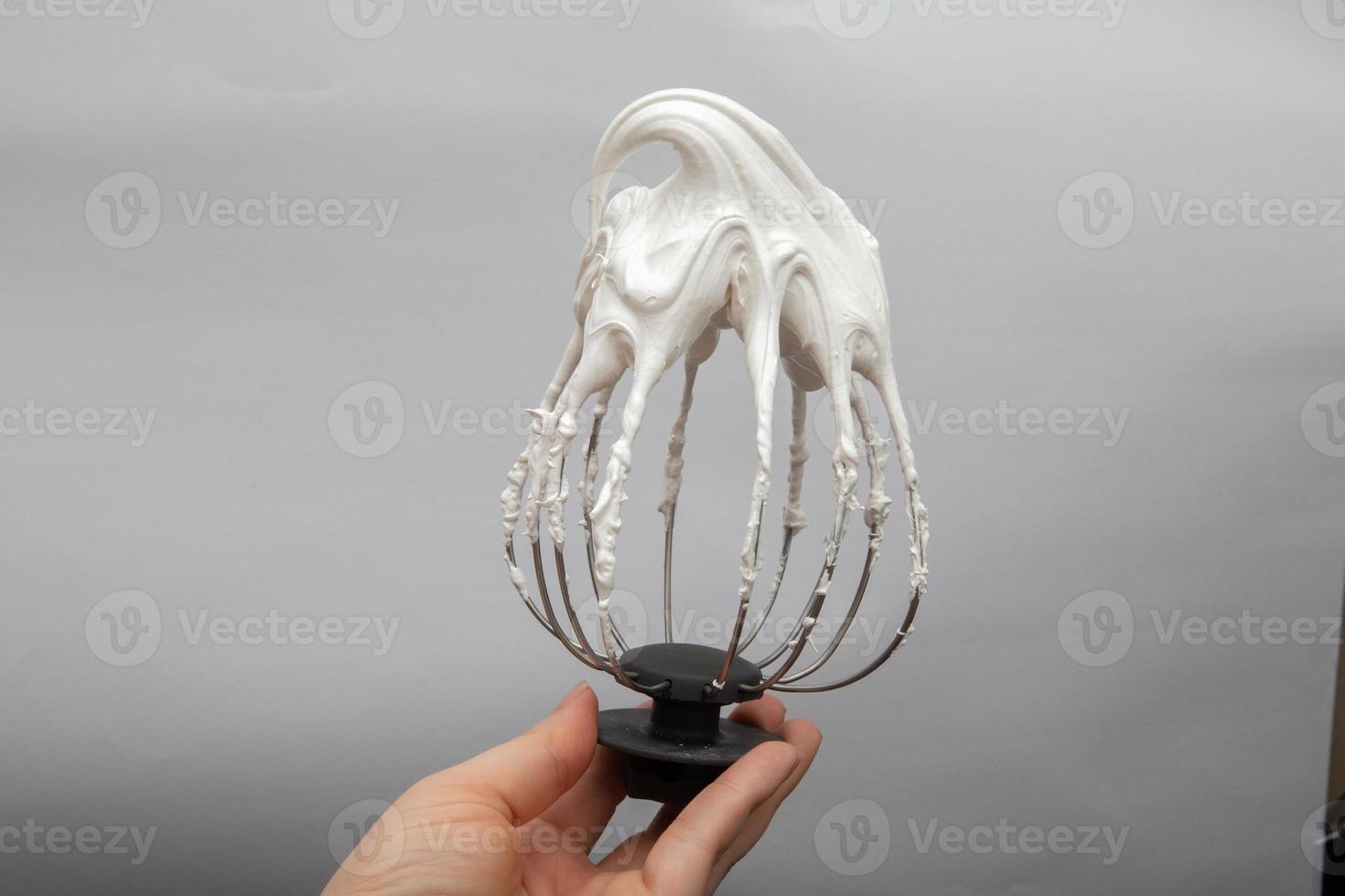 Metal whisk with whipped egg with shadows whites on white background photo