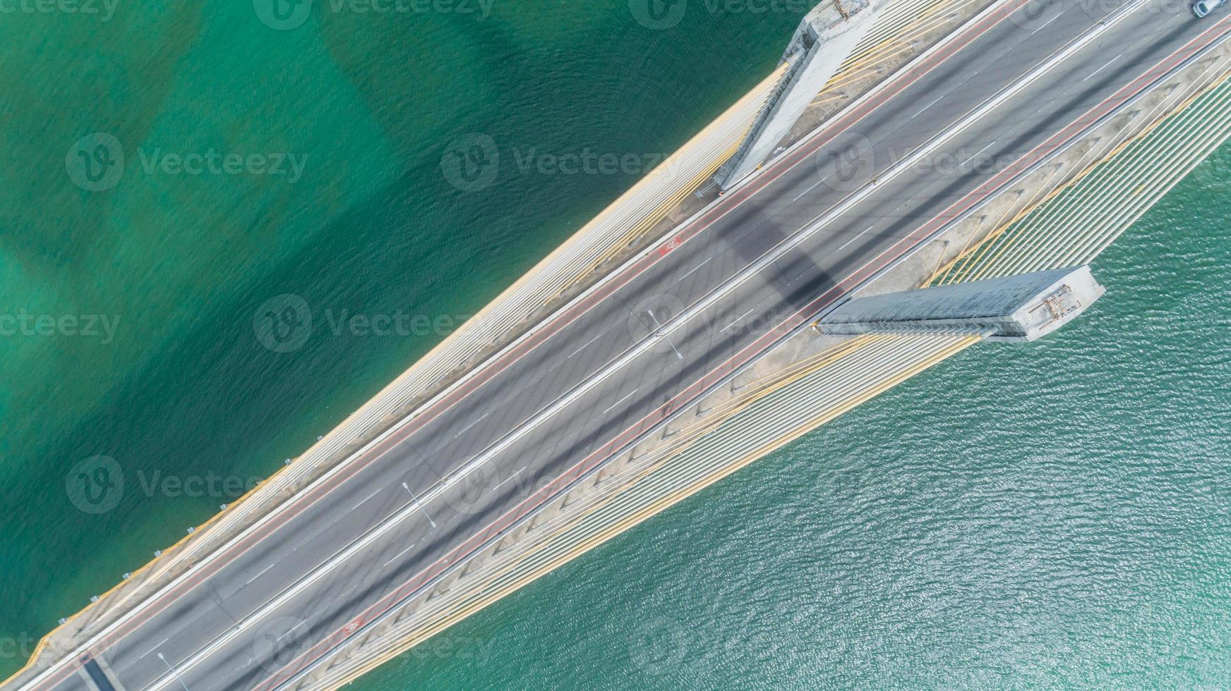Aerial view of car driving on a bridge with natural forest trees, sand, tropical beach and waves rolling into the shore. photo