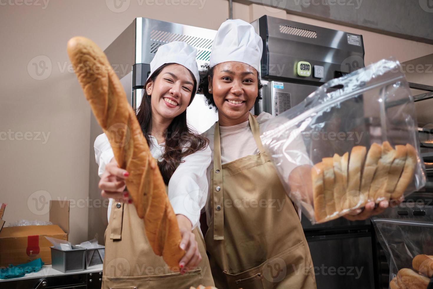 retrato de jóvenes chefs con uniformes de delantal con sombreros mirando a la cámara con una sonrisa alegre y orgullosa con pan en la cocina. amigo y socio de los alimentos de panadería y ocupación fresca de la panadería diaria. foto