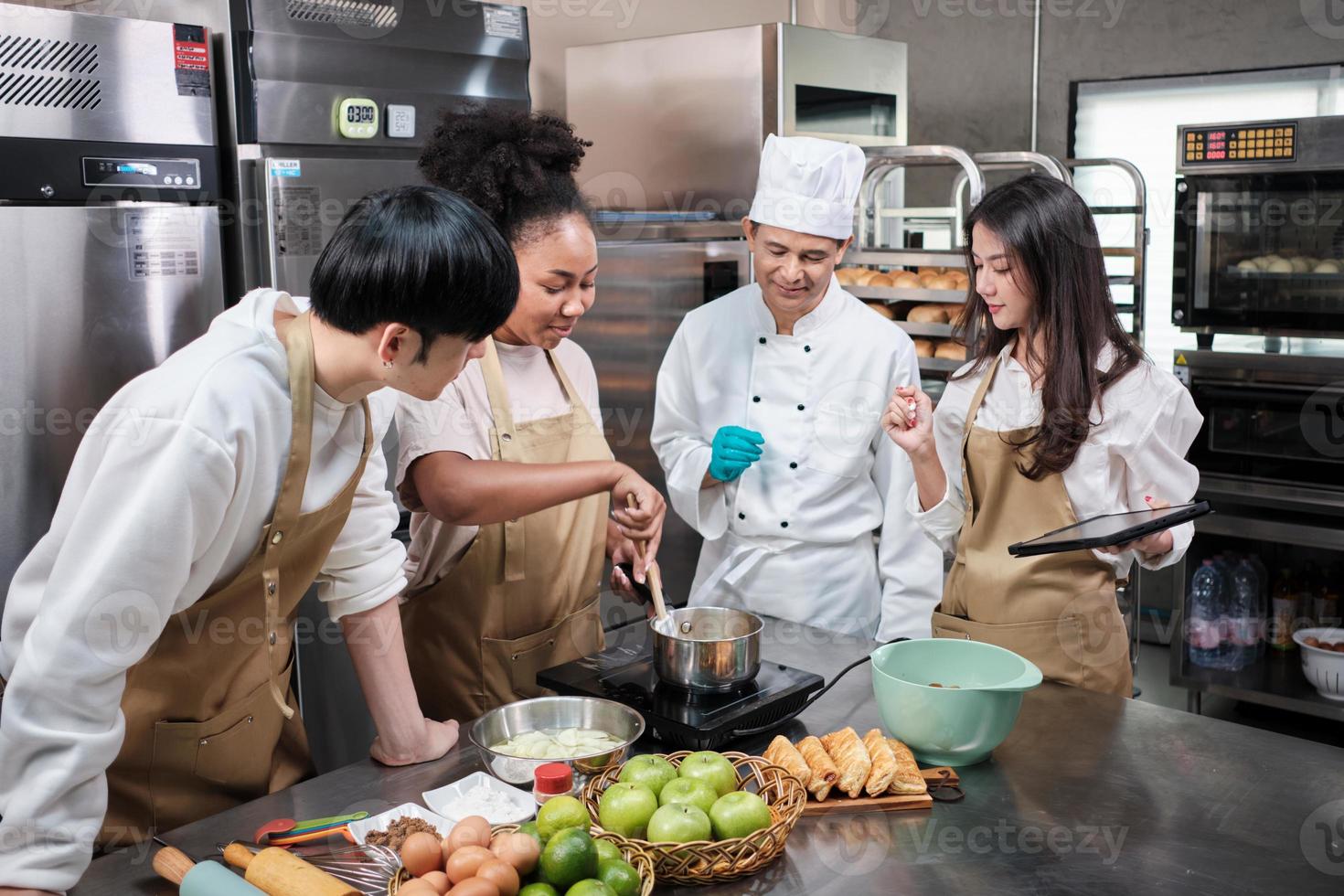 curso de cocina de hobby, chef masculino senior en uniforme de cocinero enseña a los jóvenes estudiantes de cocina a preparar, mezclar y revolver ingredientes para pasteles, pasteles de frutas en la cocina de acero inoxidable del restaurante. foto