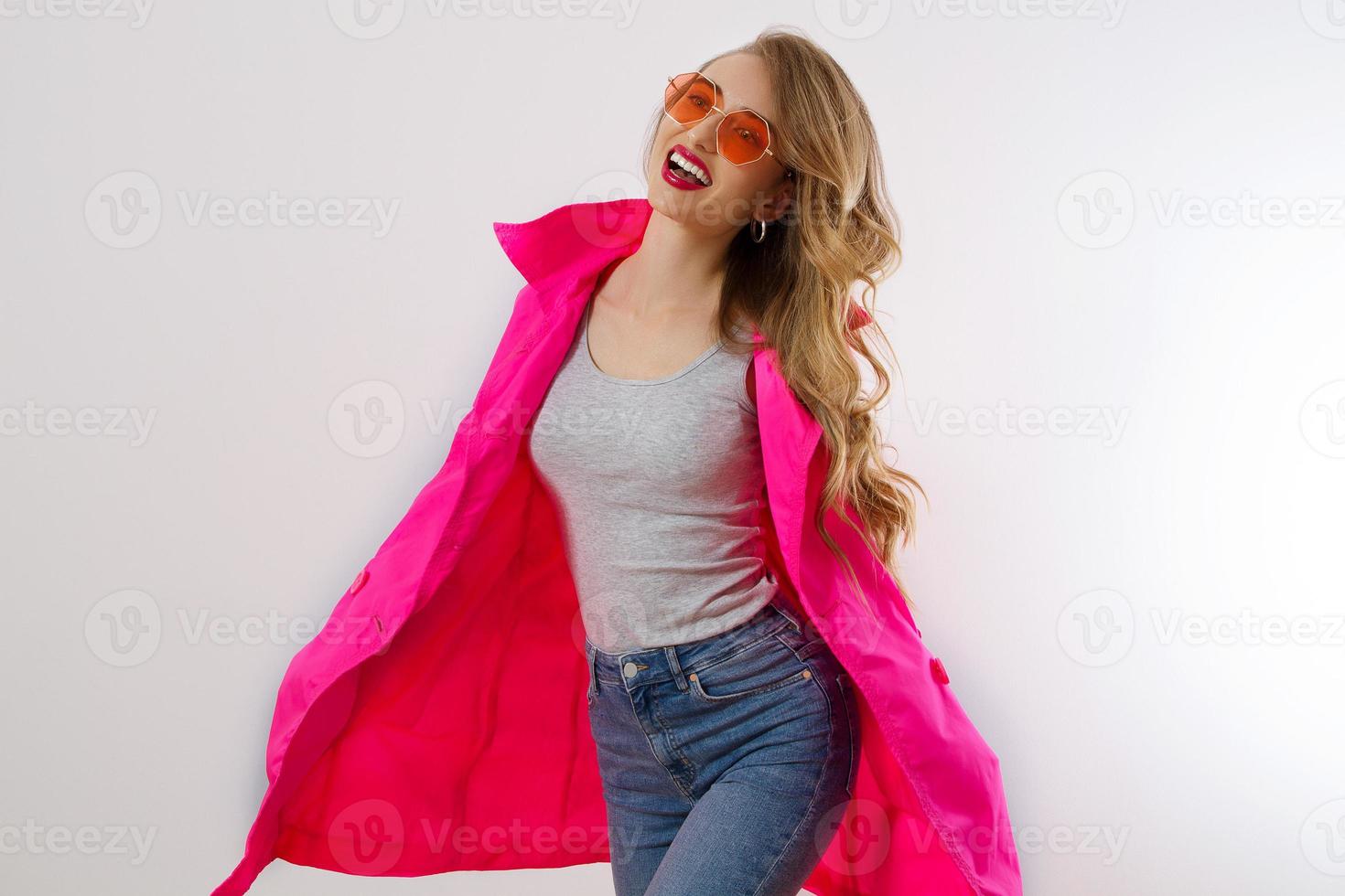 Cierra a una chica feliz con gafas de sol rojas y un abrigo rosa aislado de fondo blanco. mujer joven emocionada, conmocionada y sorprendida, traje de moda. concepto de moda y compras. cabello ondulado largo. enfoque selectivo foto