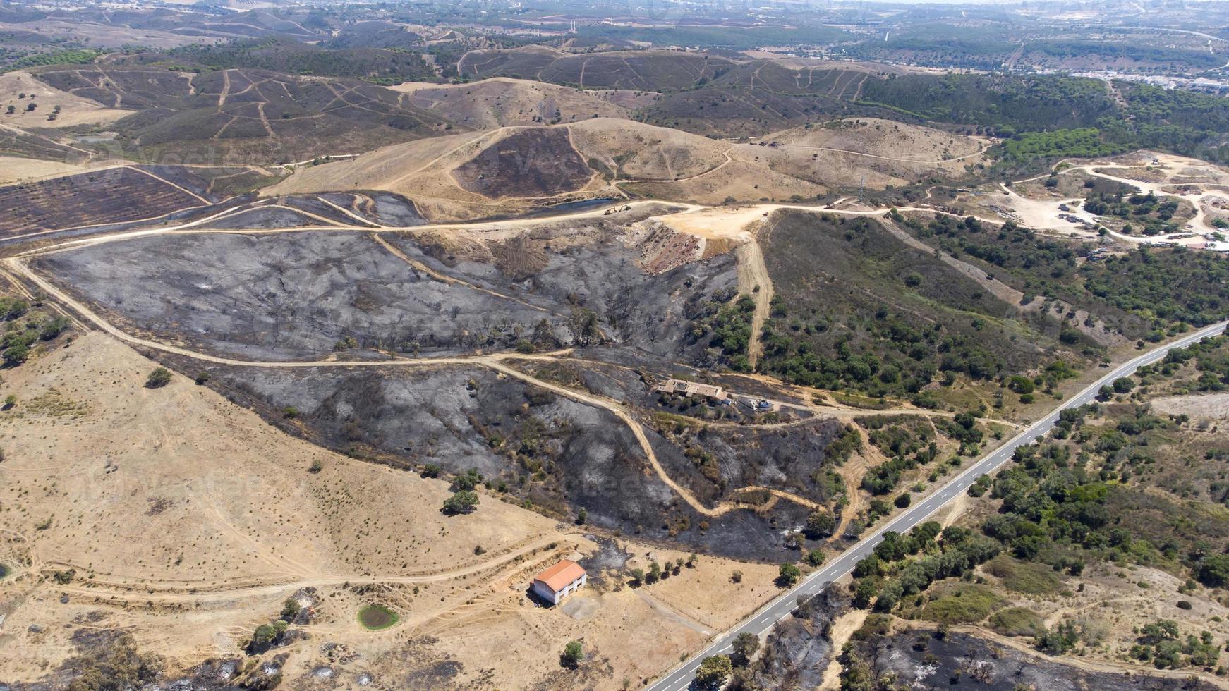 Aerial drone view of burned forest next to the road. Dark land and black trees caused by fire. Forest fire. Climate change, ecology and land. photo