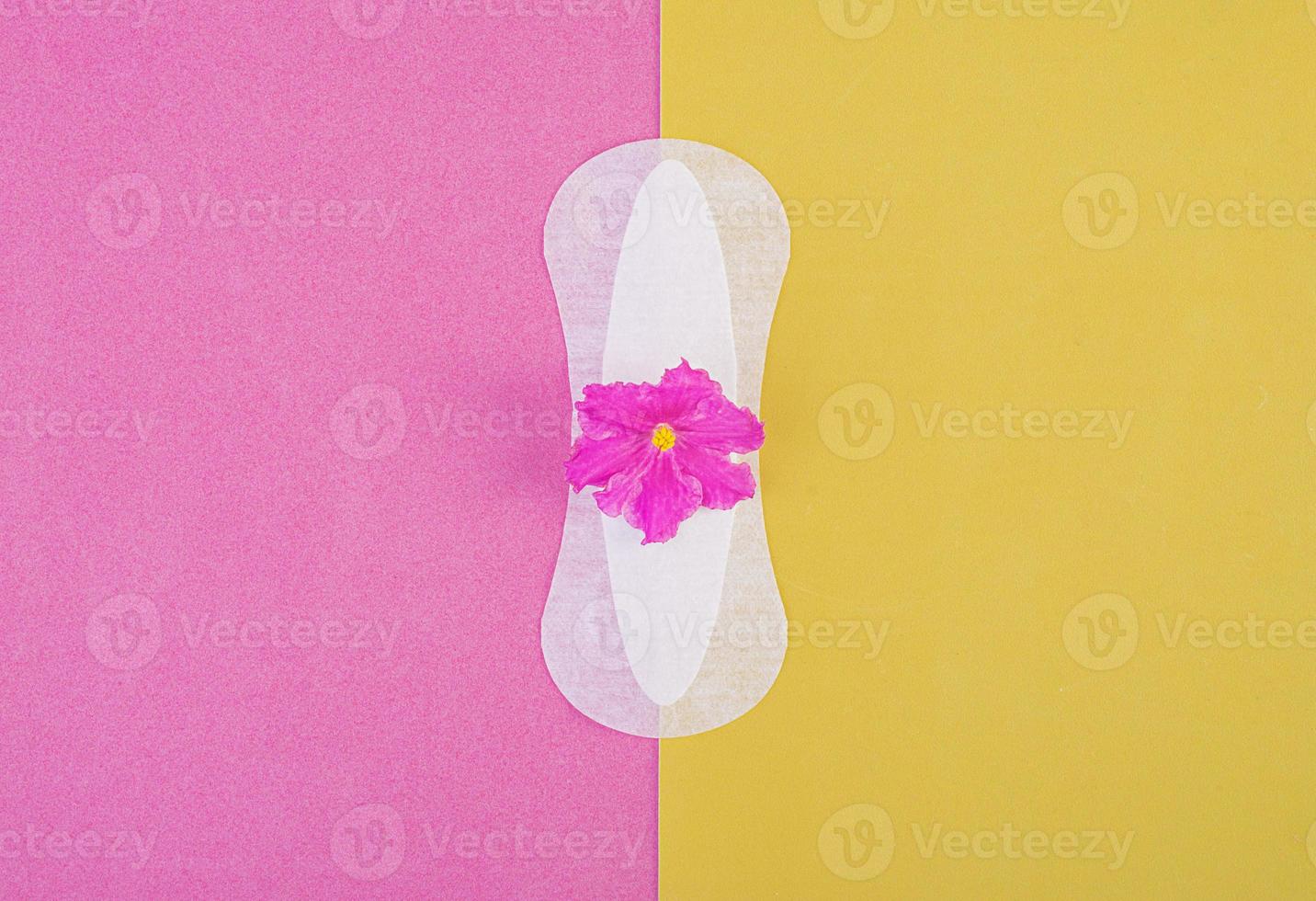 Sanitary pad for critical days and a purple flower on a pink-yellow background. Care of hygiene during menstruation. Regular menstrual cycle. Top view, copy space photo