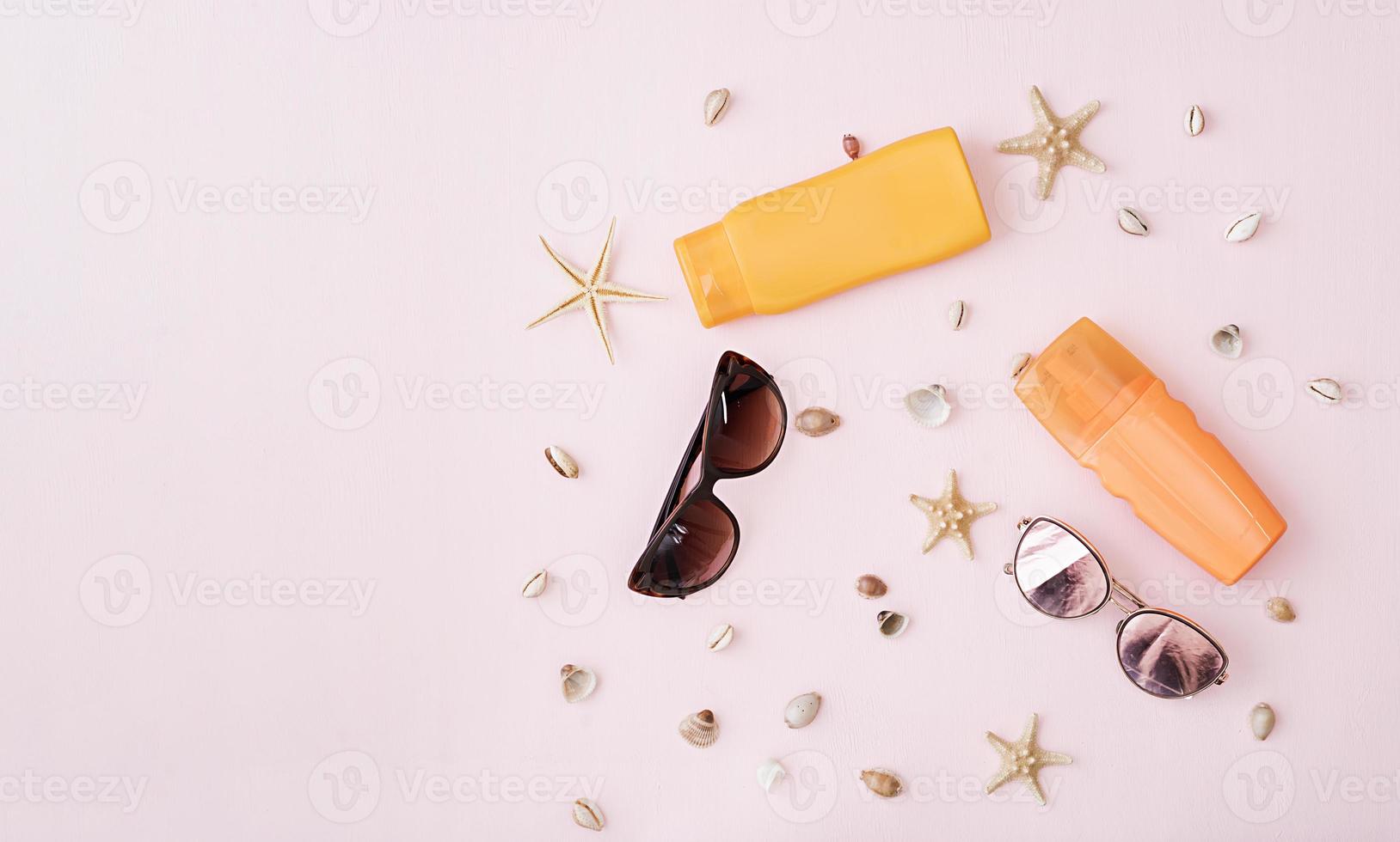 Sunglasses with sunscreen cream, defferent seashell and starfish on pink background. Top view. Flat lay photo