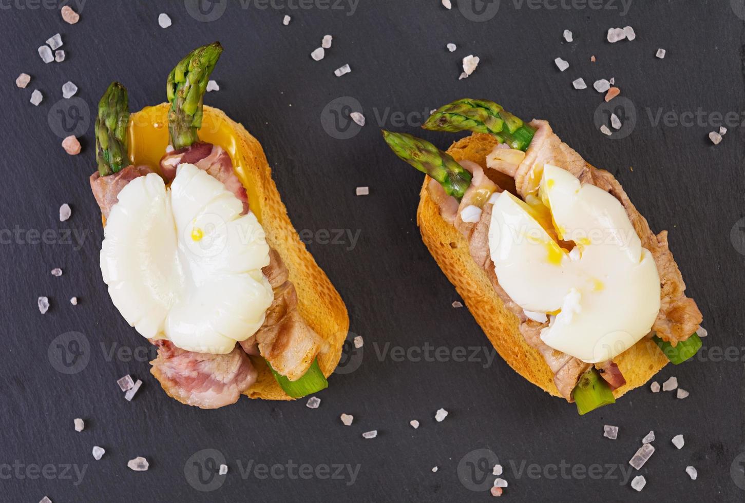 Grilled toast with asparagus in bacon and poached egg on wooden background photo