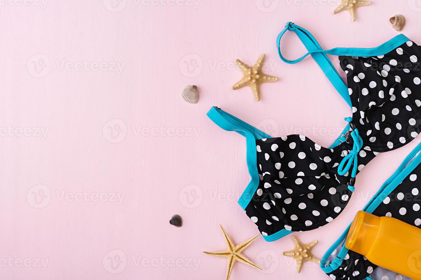 Swimsuit with different seashells and starfish on pink background. Top view photo