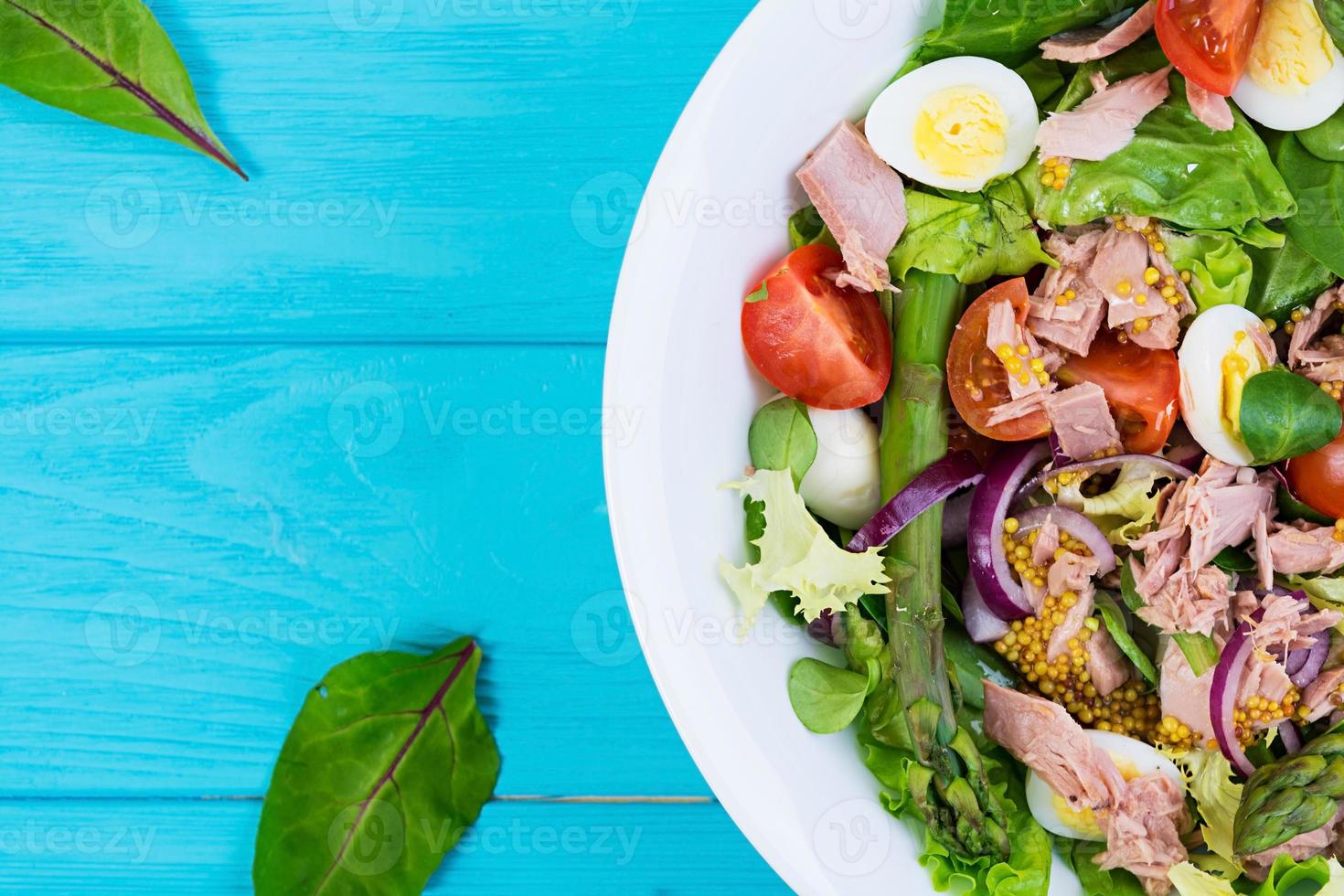 ensalada con atún, tomates, huevos de codorniz, espárragos y cebollas sobre fondo de madera foto